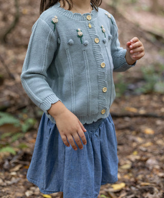Child wearing a blue knitted sweater and dress in a forest setting